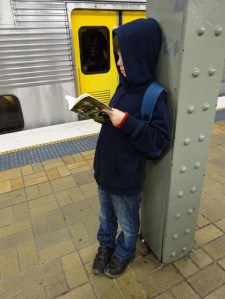 Mr. 8 reading The Mapmaker Chronicles: Prison of the Black Hawk by A. L. Tait in train station after SWF 2015